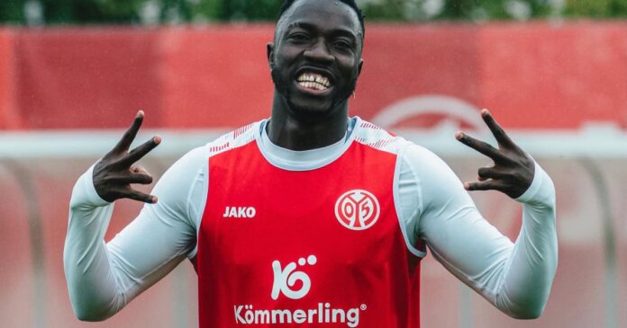 Homme souriant en tenue de sport rouge avec logos visibles sur le maillot, fond flou