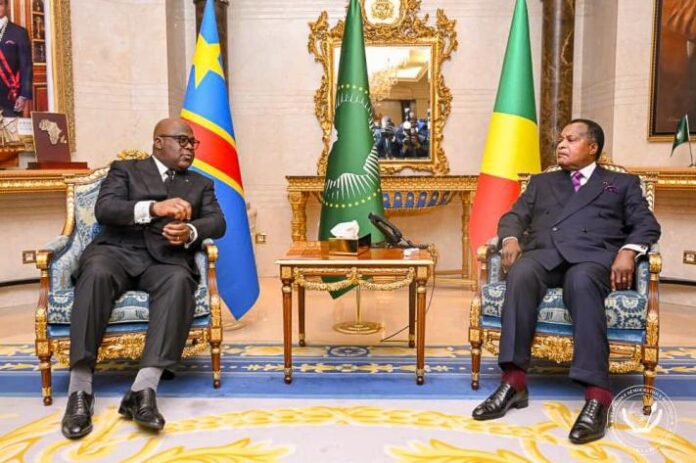 Deux drapeaux flottant au bord du fleuve Congo avec un bâtiment officiel à l'arrière-plan