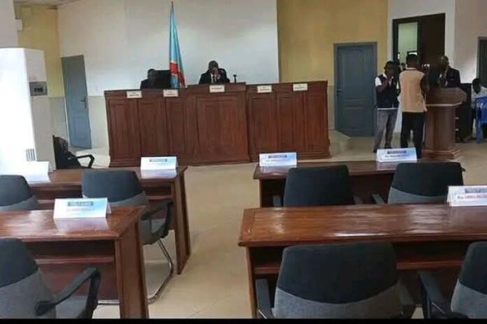 Hémicycle de l’Assemblée provinciale de la Tshuapa avec des bancs majoritairement vides et quelques dossiers sur les pupitres